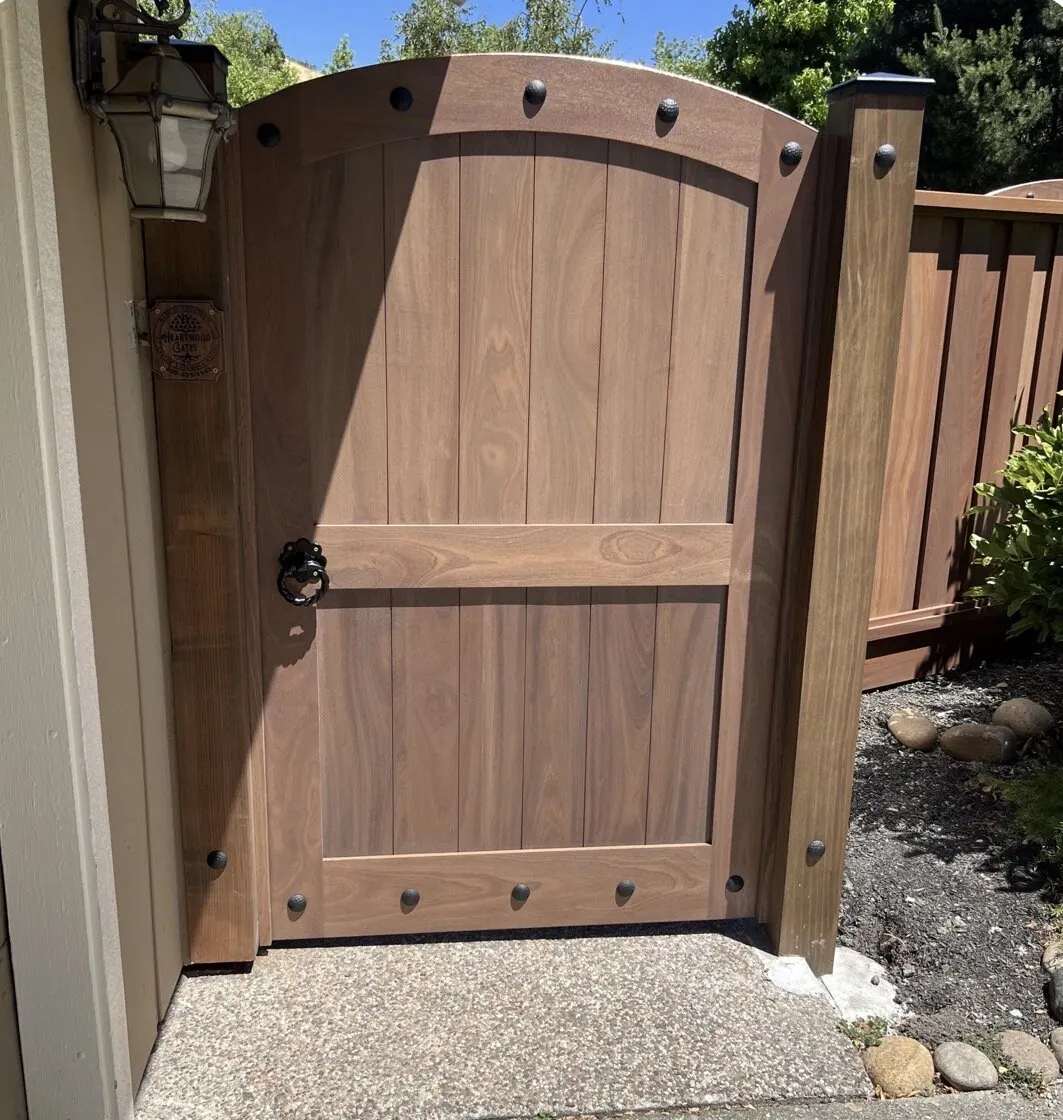 Arched mahogany side gate with iron clavos, ring pull latch and branded Heartwood Gates plaque