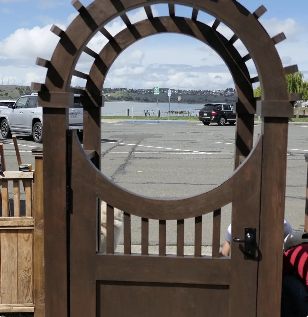 Arched mahogany pedestrian gate with large circular cutout framing a bay view